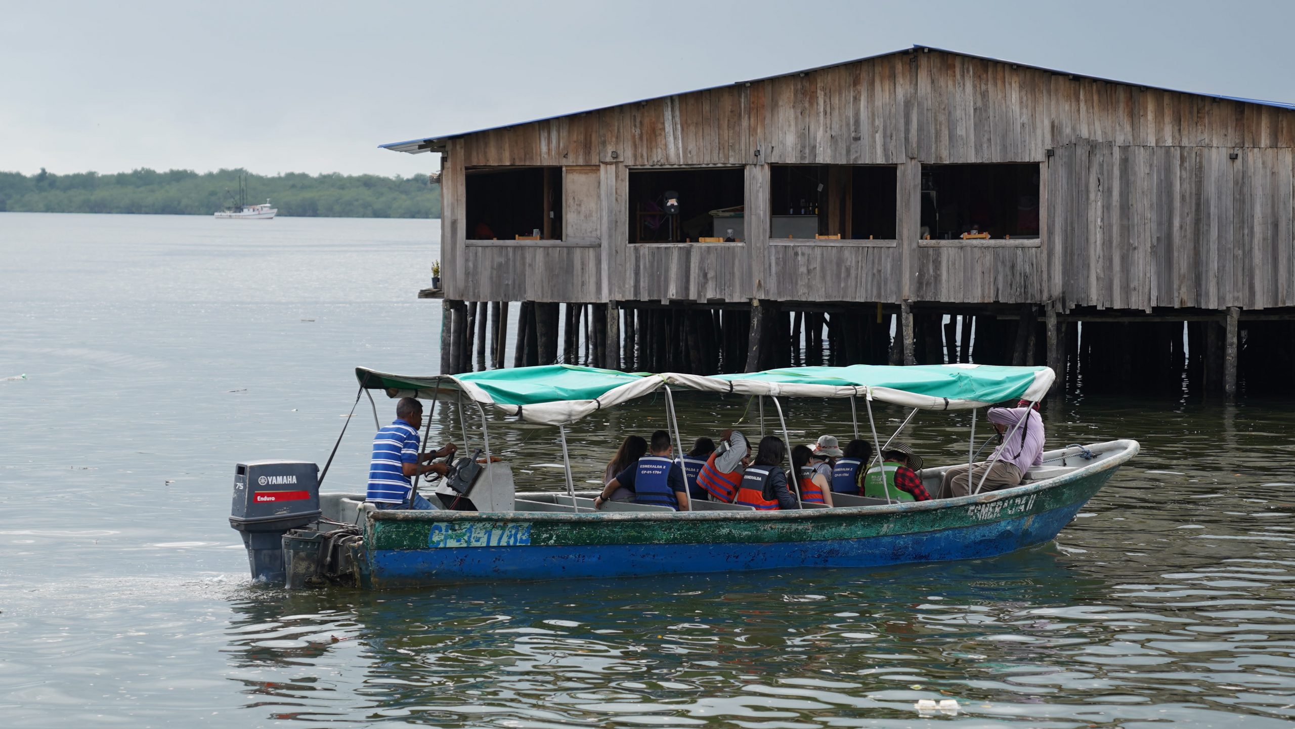 Fotografía de en la que se ve una lancha, con pasajeros, y una casa de madera en el puerto de Buenaventura