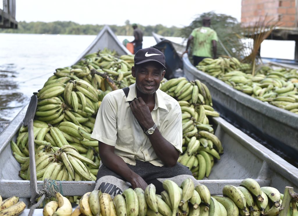 Retrato de un hombre sonriente rodeado de plátanos a bordo de su bote en el puerto de Guapi, Cauca, destacando la agricultura como fuente de sustento local